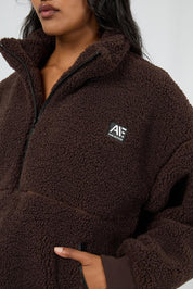 A model wearing the Amara Quarter Zip Teddy in colour Brown, from the front, showing the whole outfit