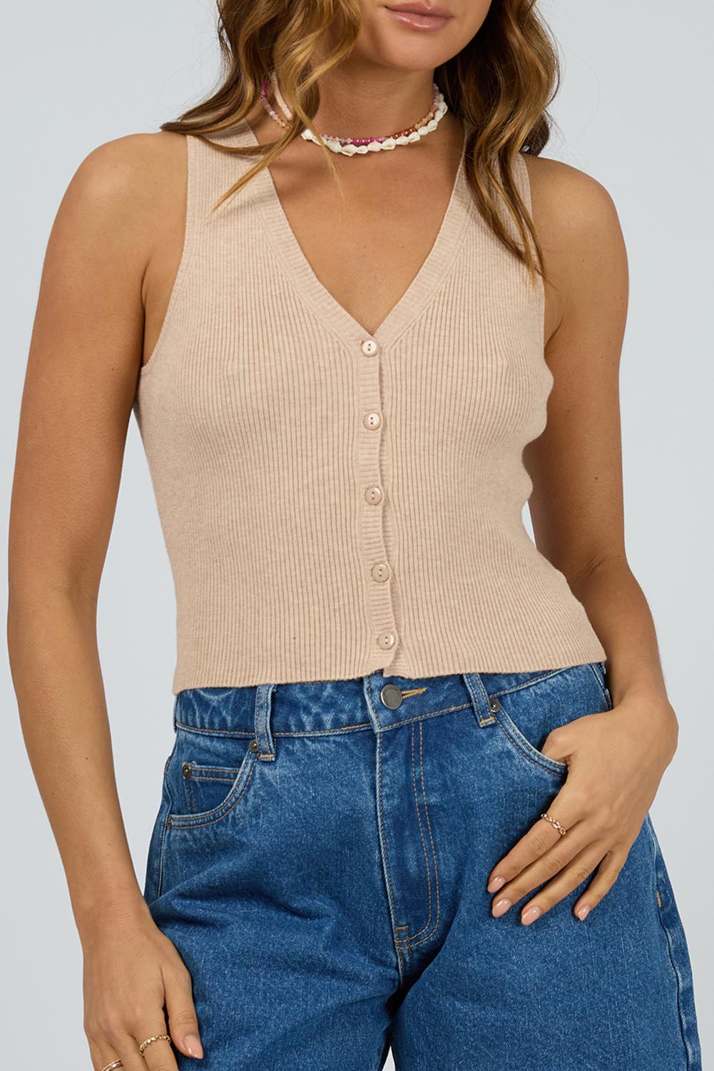 A model wearing the Henley Knit Vest in colour Oat, from the front, cropped image