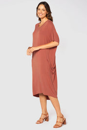 A model wearing the Samara Dress in colour Cedarwood, from the front, showing the whole outfit