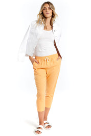 A model wearing the Lennon Pant in colour Mango, from the front, showing the whole outfit