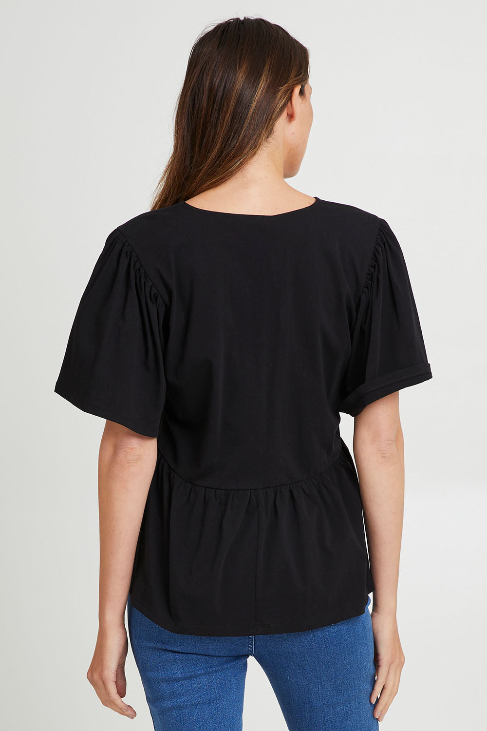 Model Madeline wearing size 10 of the Celia Tee in colour Black (Black), from the back