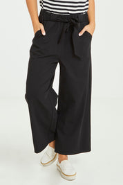 Model Tahlia wearing size 10 of the Dasha Pant in colour Black (Black), from the front, cropped image