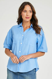 Model Madeline wearing size 10 of the Catania Linen Shirt in colour Cornflower (Blue), from the front, cropped image
