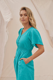 A model wearing the Whitney Dress in colour Teal (Green), from the front, showing the whole outfit