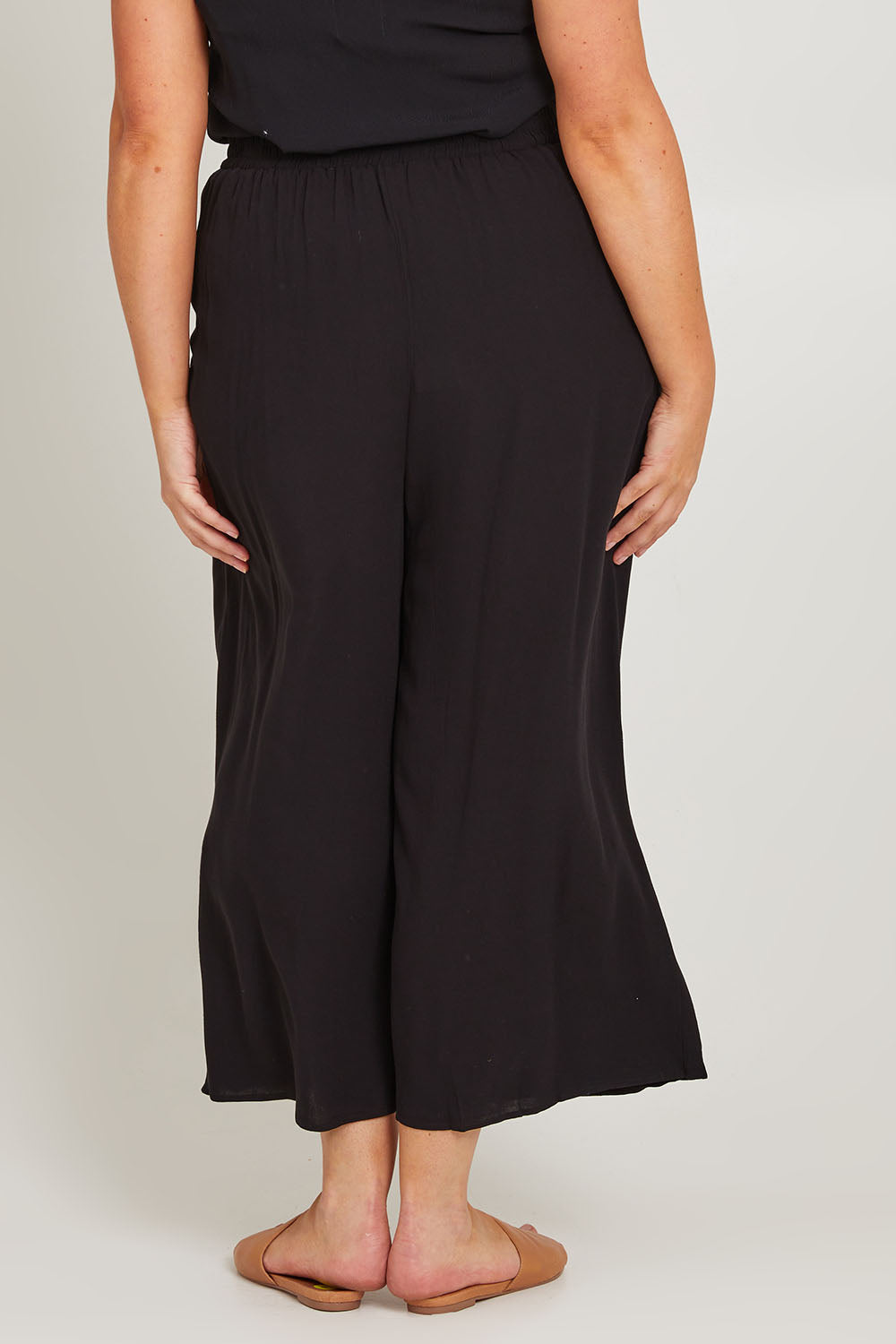 Model Poppy wearing size 16 of the Olympia Pant in colour Black (Black), from the back