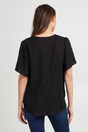 Model Madeline wearing size 10 of the Marina Linen Blouse in colour Black (Black), from the back