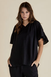 A model wearing the Vivienne Blouse in colour Black (Black), from the front, cropped image