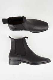 A model wearing size 37 of the Vegan Leather Pull On Flat Boot in colour Black (Black), from the front, showing the whole outfit