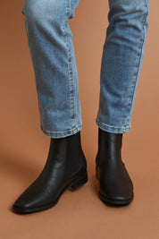 A model wearing size 39 of the Vegan Leather Pull On Flat Boot in colour Black (Black), from the front, showing the whole outfit