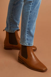 A model wearing size 39 of the Vegan Leather Pull On Flat Boot in colour Tan, from the front, showing the whole outfit