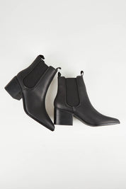 A model wearing size 37 of the Vegan Leather Pull On Heeled Boot in colour Black (Black), from the front, showing the whole outfit