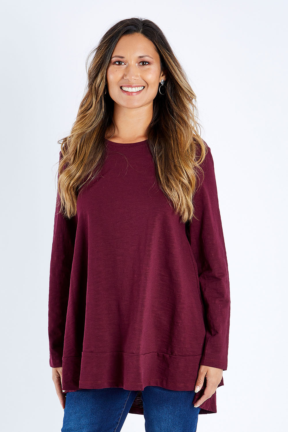 Model Kimberley wearing size 10 of The Long Sleeve Swing Tee in colour Shiraz (Red), from the front, cropped image