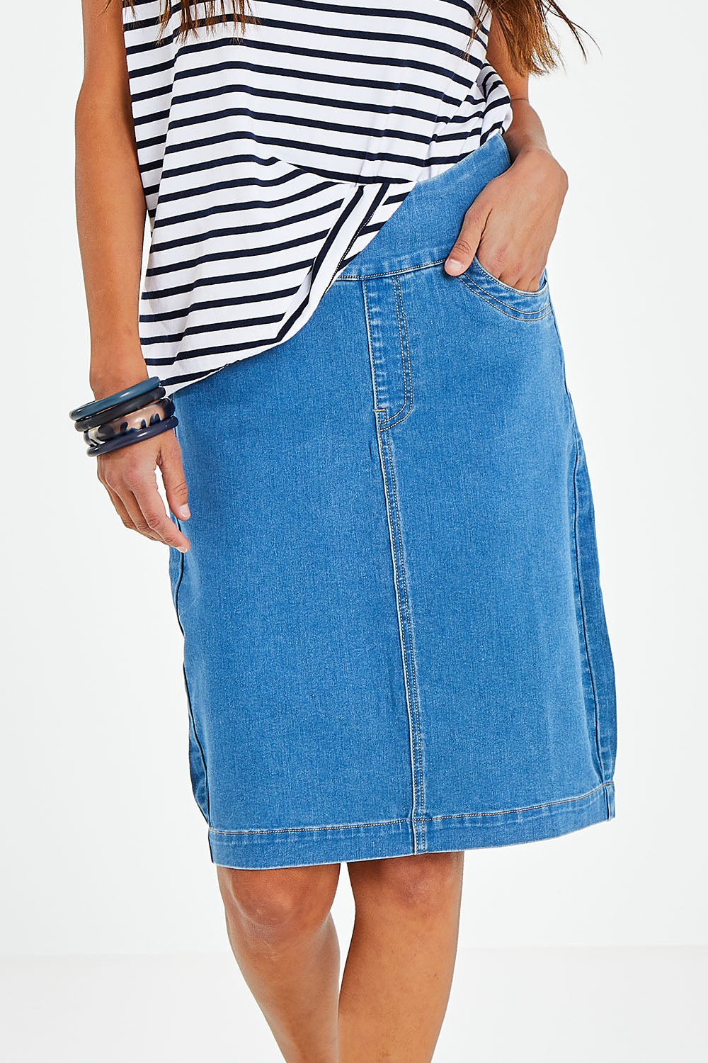 Model Vitoria wearing size 10 of The Pull On Denim Skirt in colour Middenim (Blue), from the front, cropped image