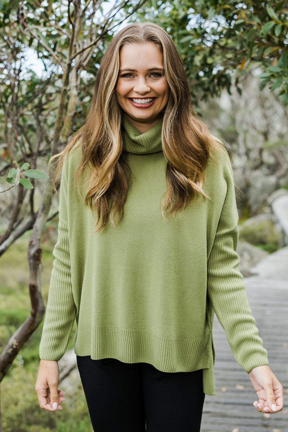 Model Tahlia wearing size S of The Essential Soft High Low Jumper in colour Avocado (Green), from the front, showing the whole outfit