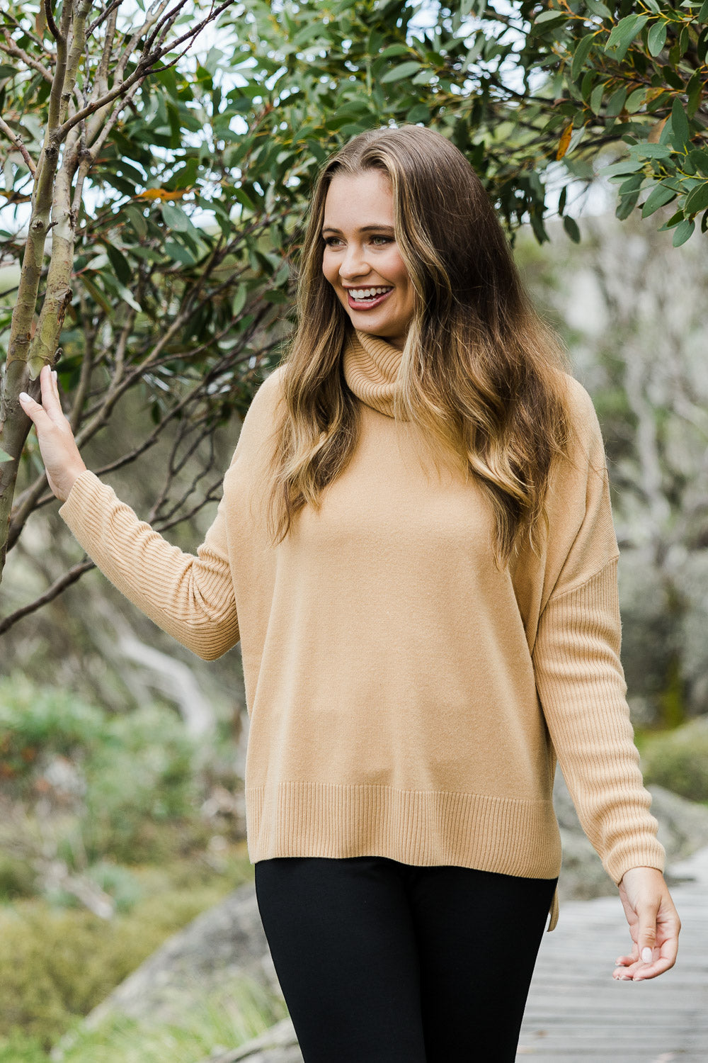 Model Tahlia wearing size S of The Essential Soft High Low Jumper in colour Camel, from the front, showing the whole outfit