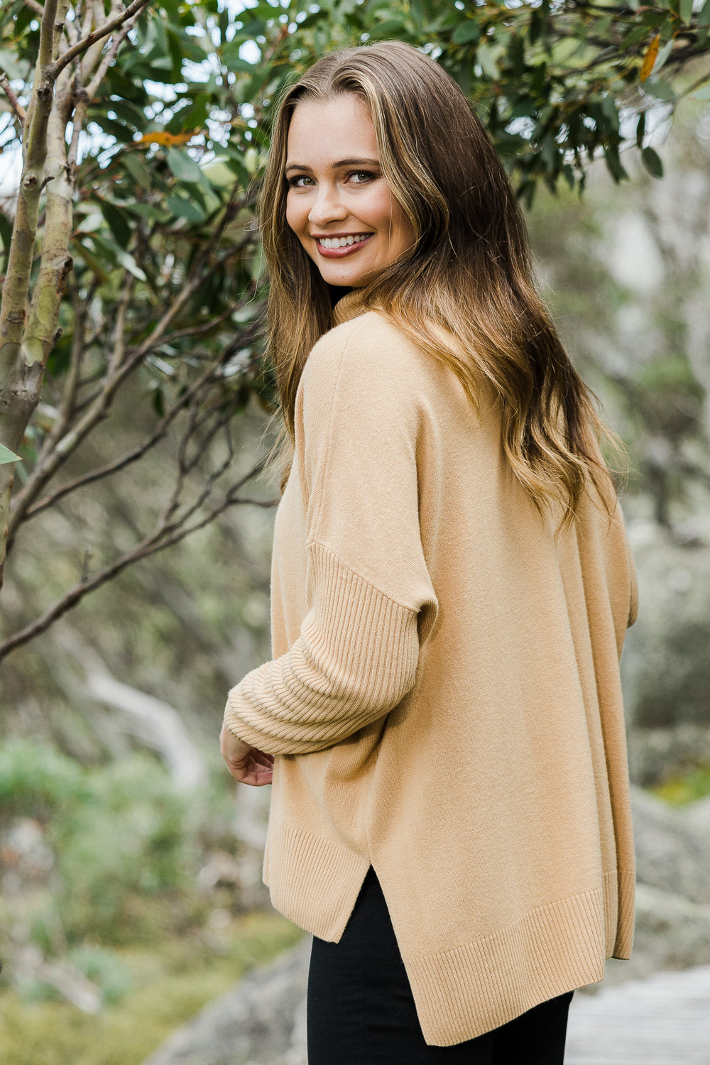 Model Tahlia wearing size S of The Essential Soft High Low Jumper in colour Camel, from the front, showing the whole outfit