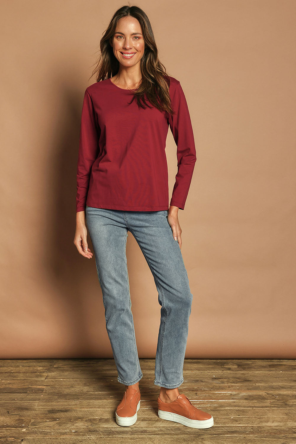 Model Madeline wearing size 10 of The Keepers Long Sleeve Tee in colour Shiraz (Red), from the front, showing the whole outfit