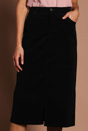 Model Madeline wearing size 10 of The 5 Pocket Cord Midi Skirt in colour Black (Black), from the front, cropped image