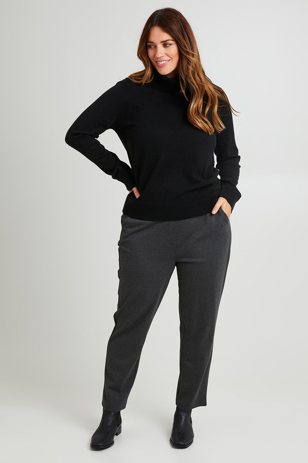 Model Laura wearing size L of The Keepers Soft Roll Neck Jumper in colour Black (Black), from the front, showing the whole outfit