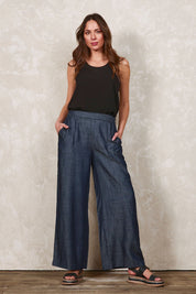 Model Madeline wearing size 10 of The Luxe Chambray Pull On Pant in colour Darkdenim (Blue), from the front, showing the whole outfit
