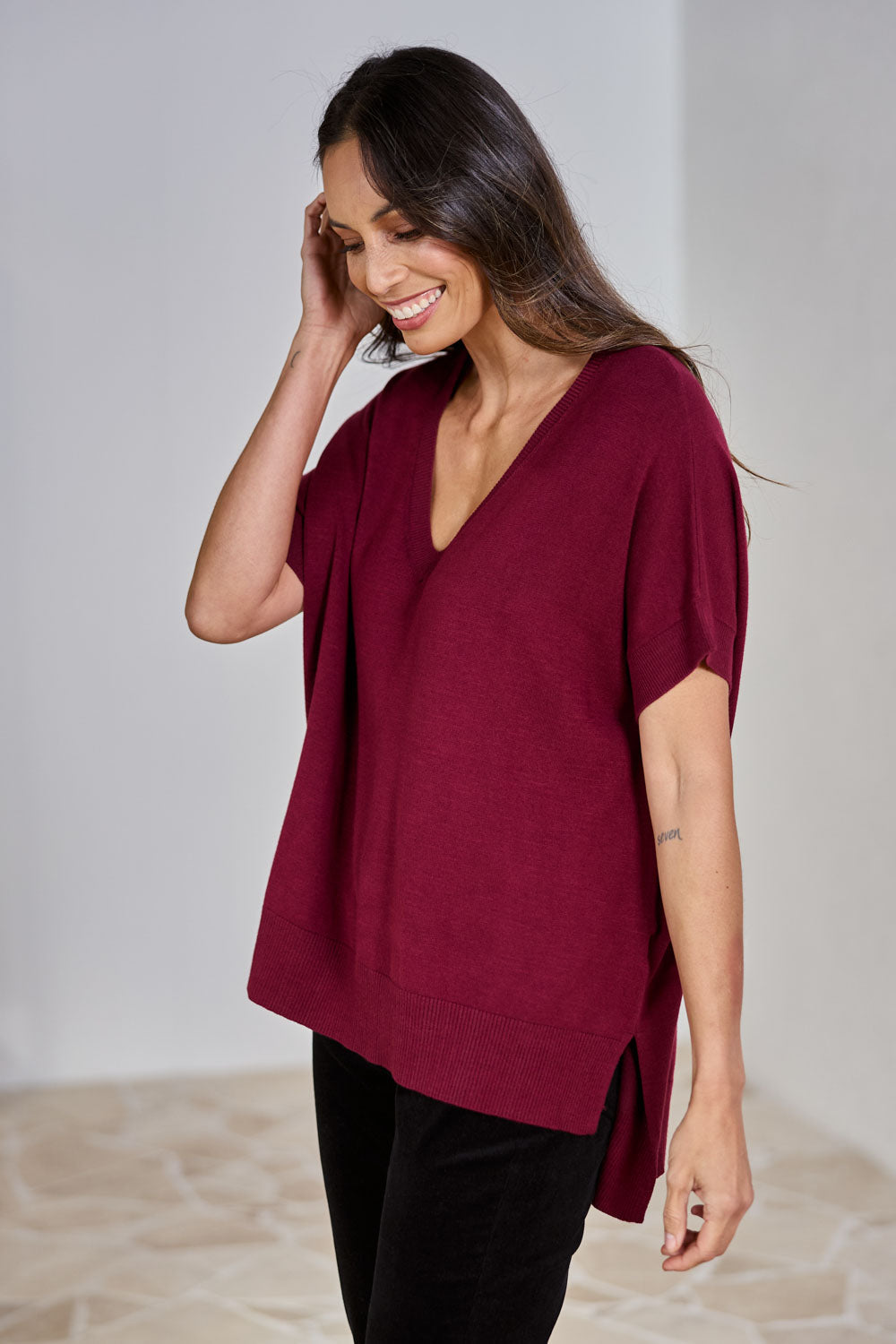 Model Amanda wearing size S of The All Season V Neck High Low Tee in colour Sangria (Red), from the front, showing the whole outfit