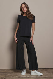 Model Madeline wearing size 10 of The Pack & Go Luxe Bamboo Wide Leg Pant in colour Black (Black), from the front, showing the whole outfit