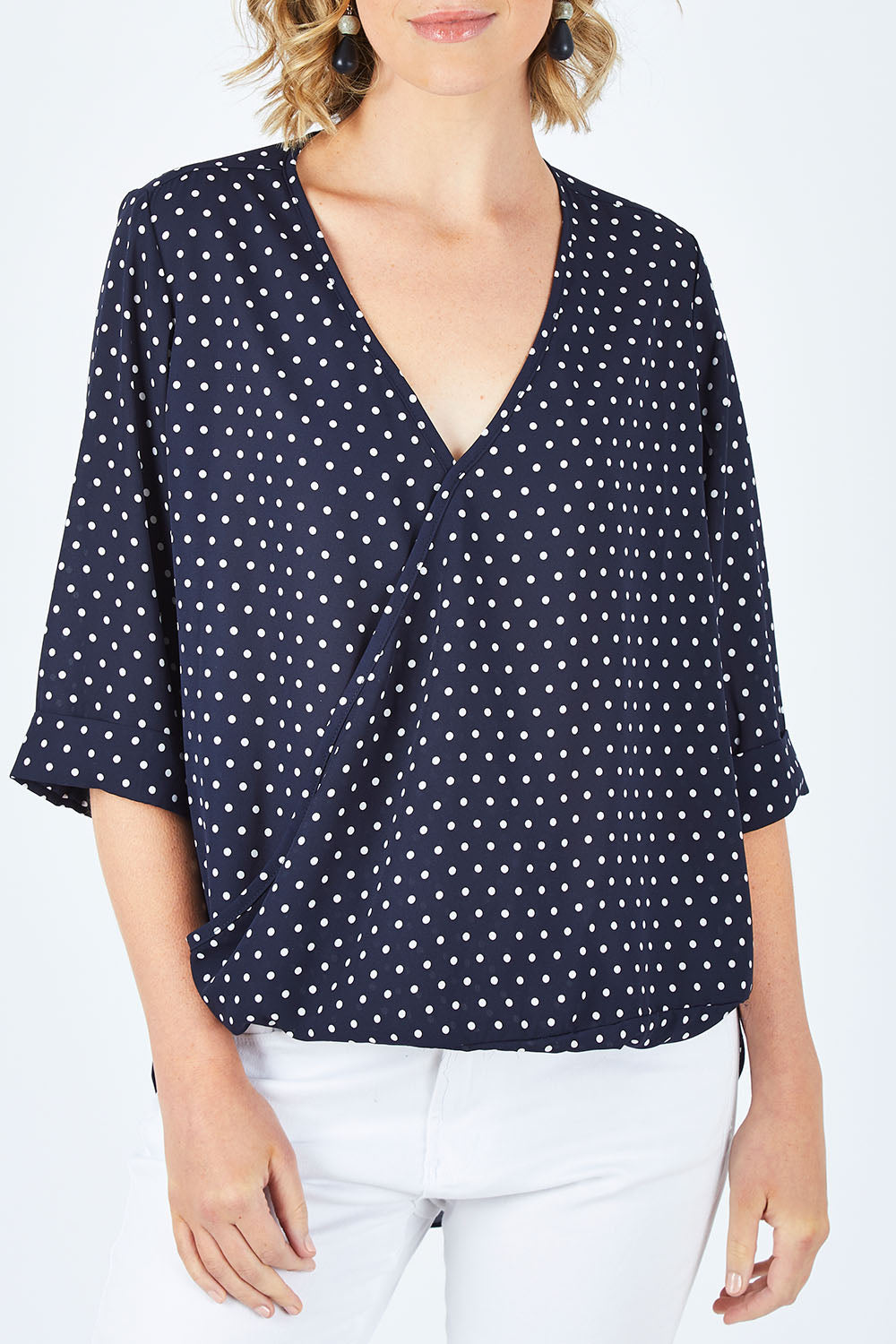 Model Chelsea wearing size 10 of The Cross Front Spot Blouse in colour NavySpot (Blue), from the front, cropped image
