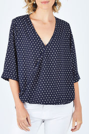 Model Chelsea wearing size 10 of The Cross Front Spot Blouse in colour NavySpot (Blue), from the front, cropped image