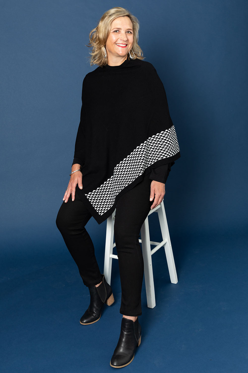 A model wearing size M-L of The Patterned Removable Roll Neck Poncho in colour Blackprint (Black), from the front, showing the whole outfit