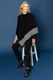 A model wearing size M-L of The Patterned Removable Roll Neck Poncho in colour Blackprint (Black), from the front, showing the whole outfit