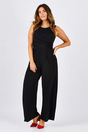 Model Laura wearing size 12 of The Cross Waist Jumpsuit in colour Black (Black), from the front, showing the whole outfit
