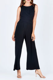 Model Rebecca wearing size 10 of The Cross Waist Jumpsuit in colour Black (Black), from the front, cropped image