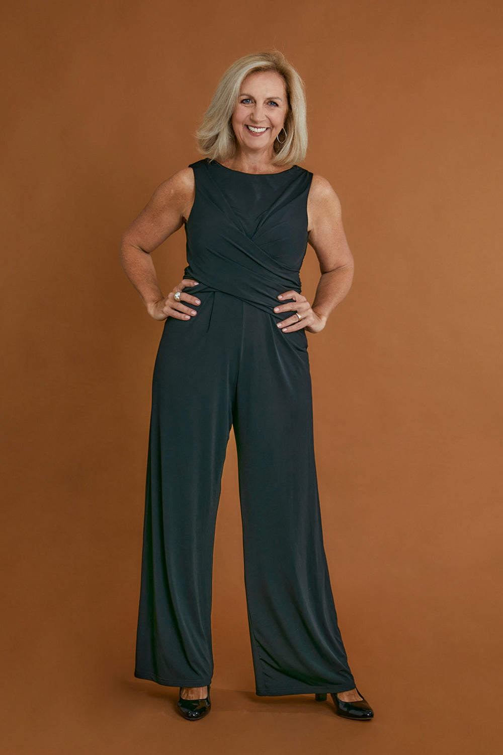 Model Sandy wearing size 10 of The Cross Waist Jumpsuit in colour Black (Black), from the front, showing the whole outfit
