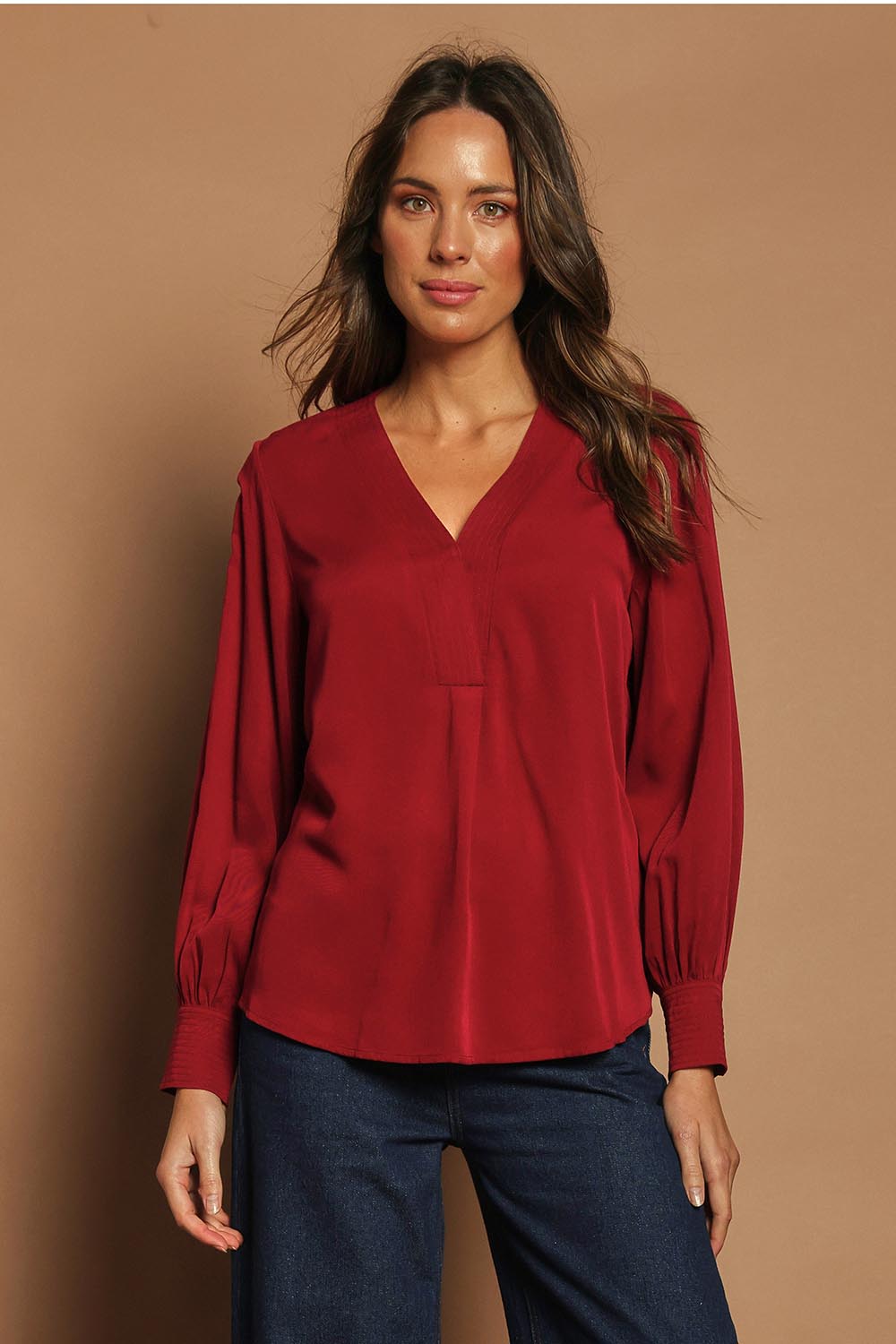 Model Madeline wearing size 10 of The Button Detail Cuff Blouse in colour Garnet (Red), from the front, showing the whole outfit