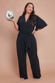 Model Ashleigh wearing size 16 of The Bell Sleeve Jumpsuit in colour Black (Black), from the front, showing the whole outfit
