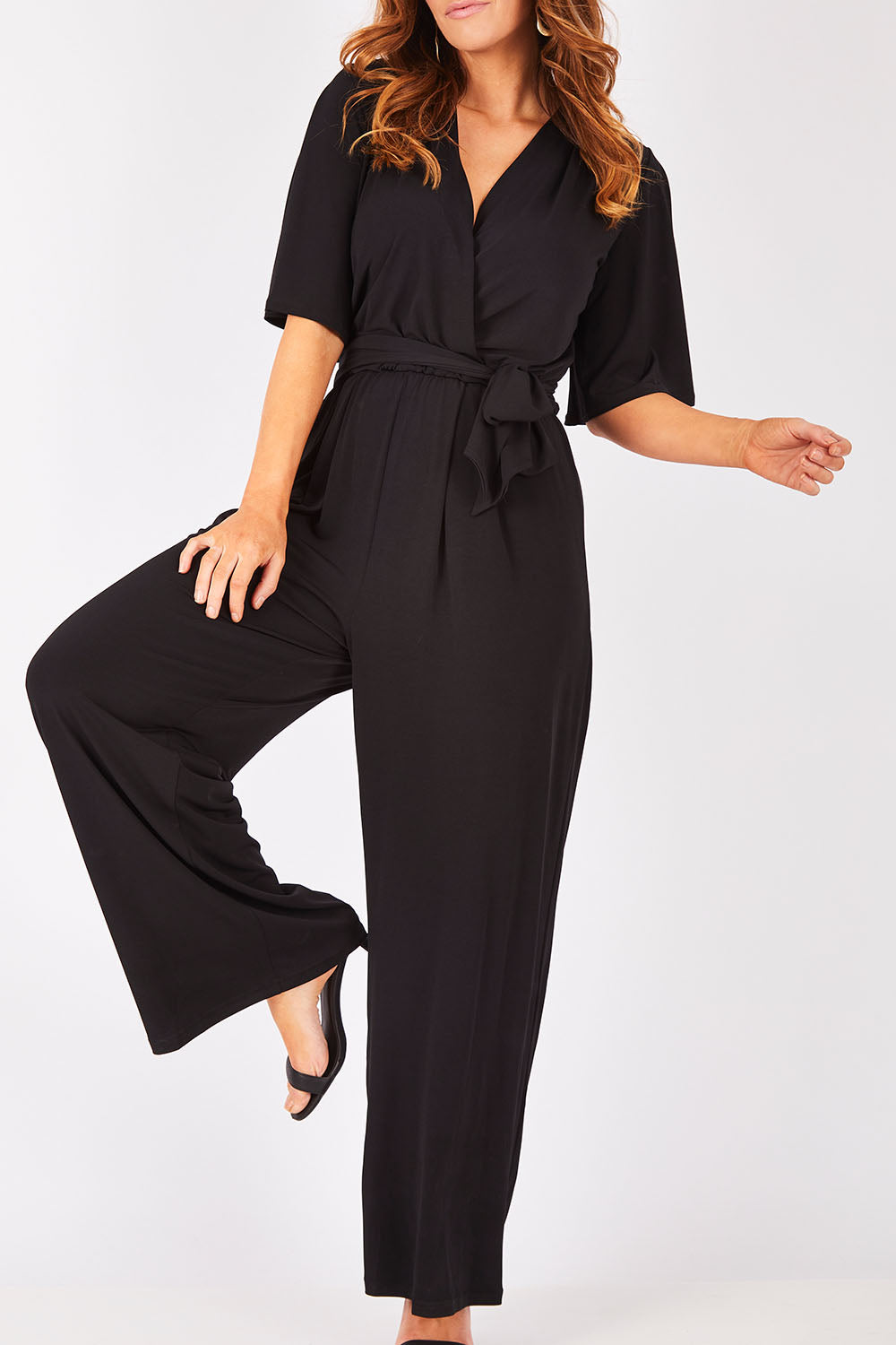 Model Laura wearing size 12 of The Bell Sleeve Jumpsuit in colour Black (Black), from the front, cropped image