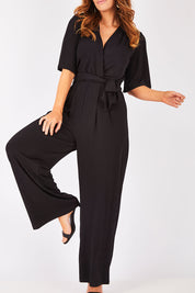 Model Laura wearing size 12 of The Bell Sleeve Jumpsuit in colour Black (Black), from the front, cropped image