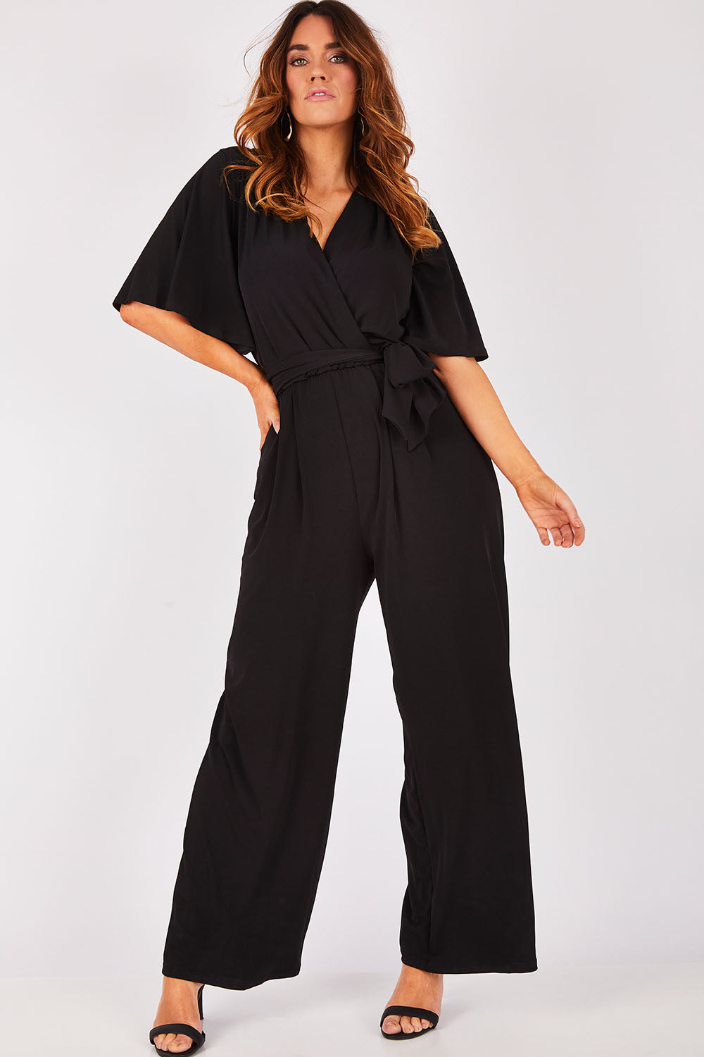 Model Laura wearing size 12 of The Bell Sleeve Jumpsuit in colour Black (Black), from the front, showing the whole outfit