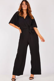 Model Laura wearing size 12 of The Bell Sleeve Jumpsuit in colour Black (Black), from the front, showing the whole outfit