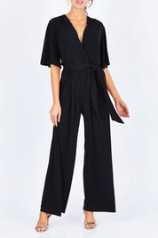 Model Madeline wearing size 10 of The Bell Sleeve Jumpsuit in colour Black (Black), from the front, cropped image