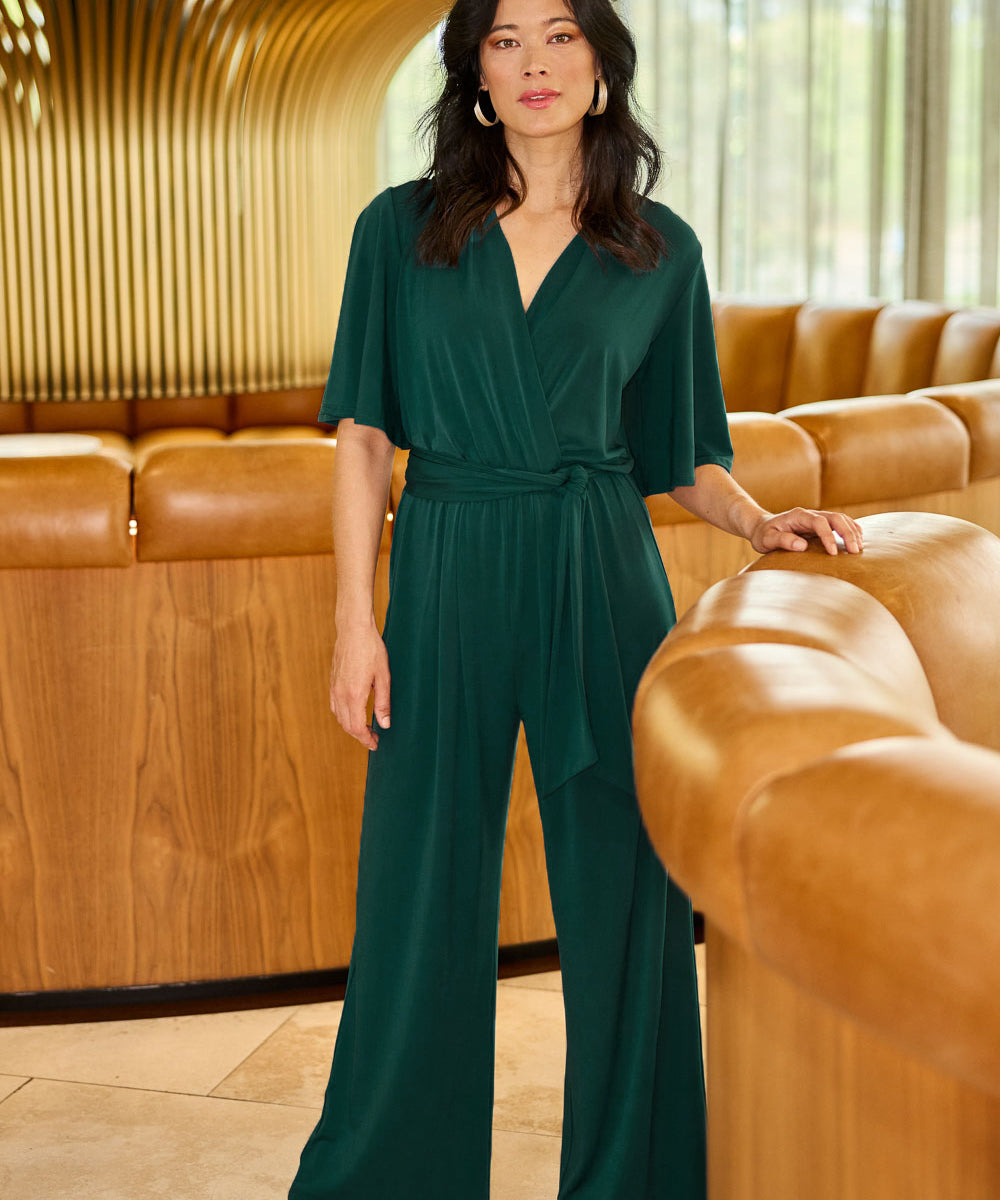 Model Miranda wearing size 10 of The Bell Sleeve Jumpsuit in colour Pine (Green), from the front, showing the whole outfit