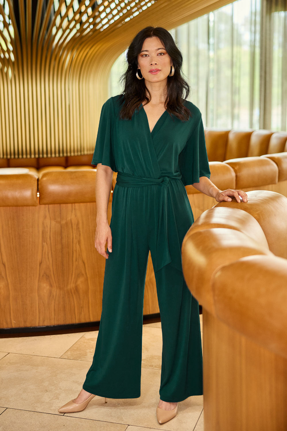 Model Miranda wearing size 10 of The Bell Sleeve Jumpsuit in colour Pine (Green), from the front, showing the whole outfit