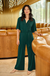 Model Miranda wearing size 10 of The Bell Sleeve Jumpsuit in colour Pine (Green), from the front, showing the whole outfit