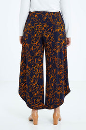 Model Sasha-Lee wearing size 16 of The Printed Cross Over Pant in colour Navyfloral (Blue), from the back