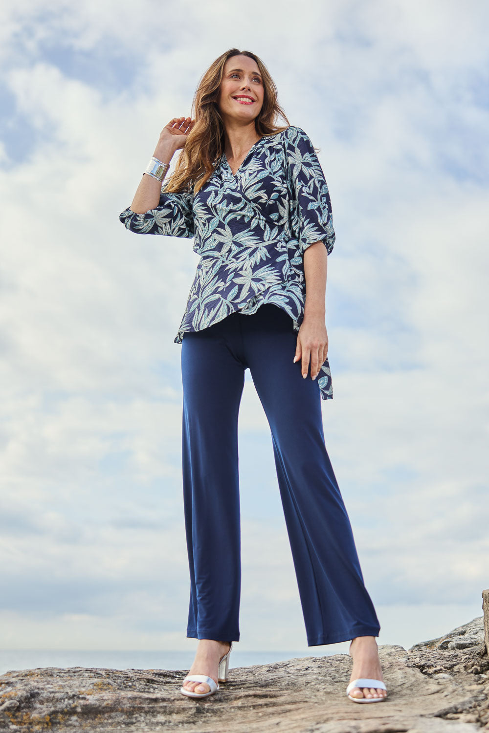 Model Clementine wearing size 10 of The Printed Blouson Sleeve Wrap Blouse in colour Navyleaf (Blue), from the front, showing the whole outfit