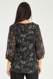 Model Stacey wearing size 10 of The Lined V Neck Blouse in colour Vines (Black), from the back