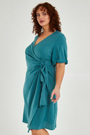 Model Maddy wearing size 16 of The Buckle Detail Faux Wrap Dress in colour Lagoon (Green), from the front, cropped image