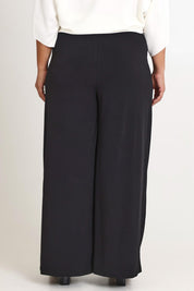 Model Ashleigh wearing size 16 of The Palazzo Jersey Pull On Pant in colour Black (Black), from the back