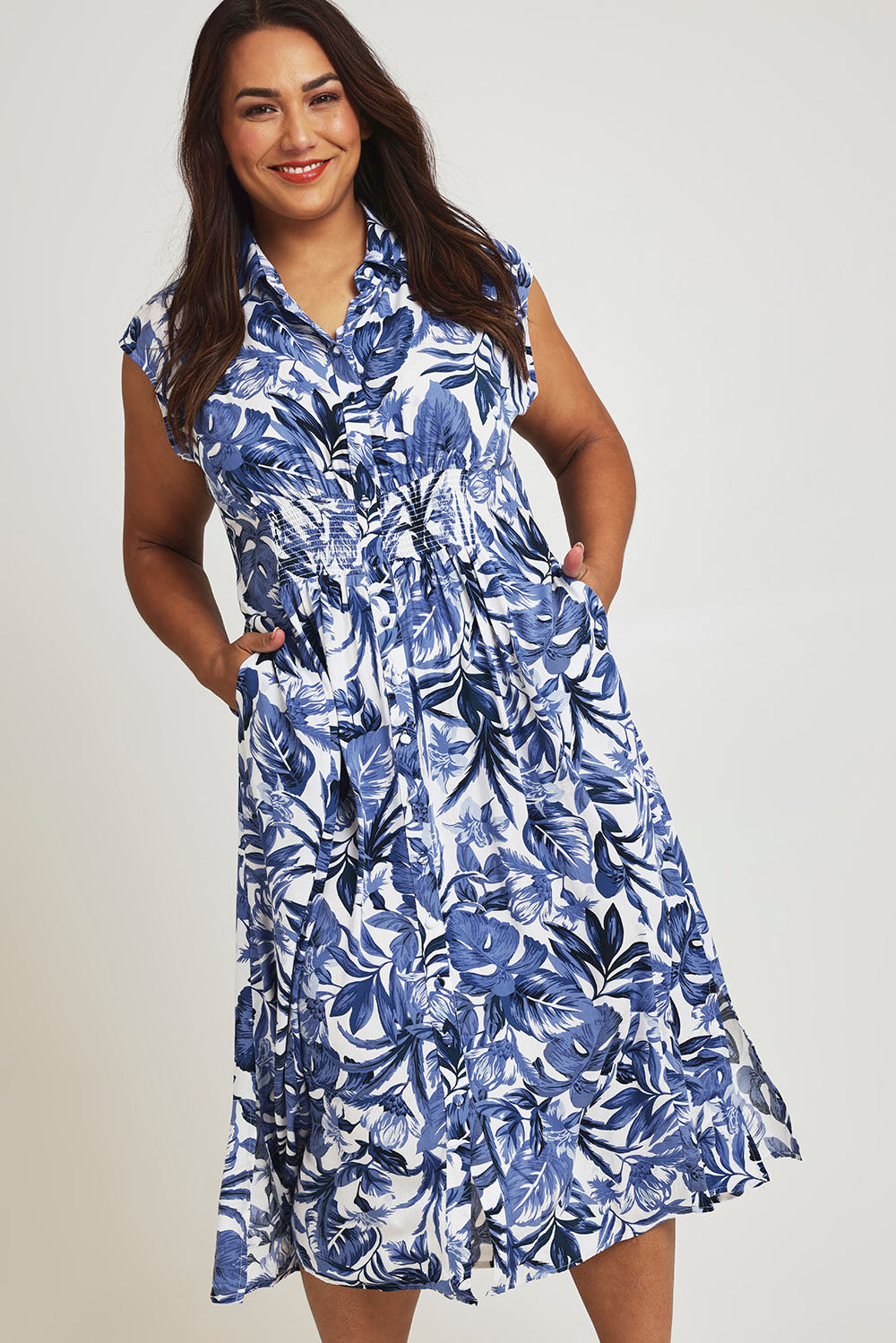 Model Ashleigh wearing size 16 of The Shirred Waist Button Through Dress in colour Tropics (Blue), from the front, cropped image