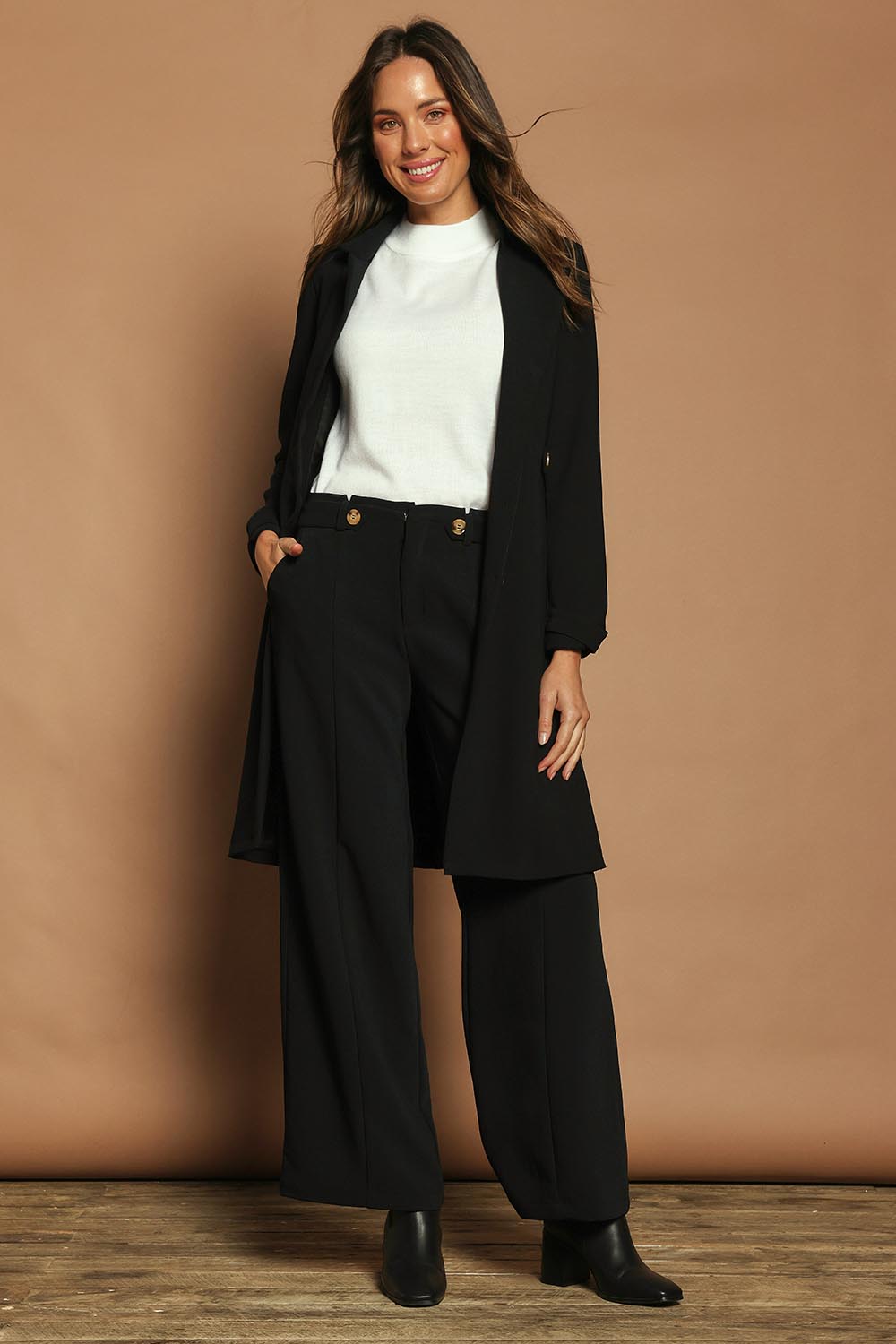 Model Madeline wearing size 10 of The Tab Detail Tailored Longline Coat in colour Black (Black), from the front, showing the whole outfit